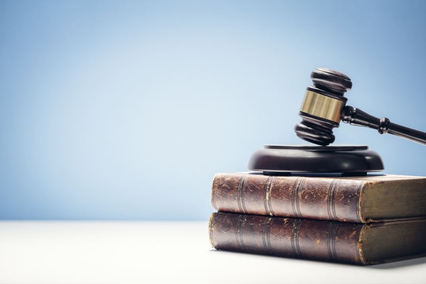A judge's gavel rests on a stack of two leather-bound law books against a blue background, conveying authority and justice.