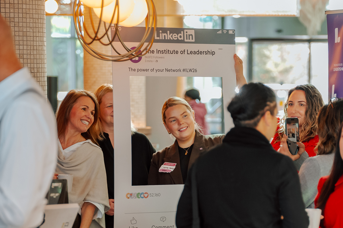 Group of people at an event holding a large Instagram-style photo frame labeled "LinkedIn" with smiles and posing for pictures, creating a lively and cheerful atmosphere.
