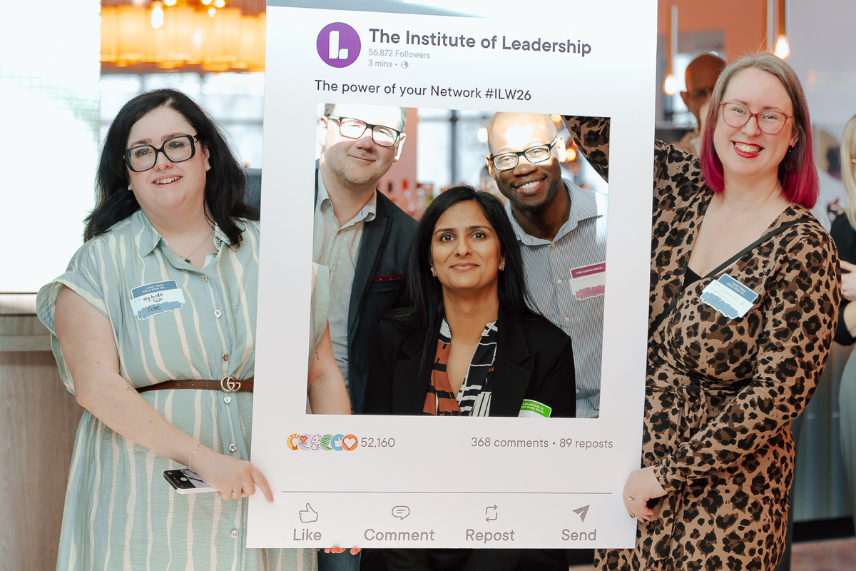A group of smiling individuals at a networking event holds a large Instagram-style frame from "The Institute of Leadership." The atmosphere is friendly and engaging.