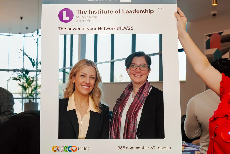 Two professionals posing in a cardboard International Leadership Week 2026 frame
