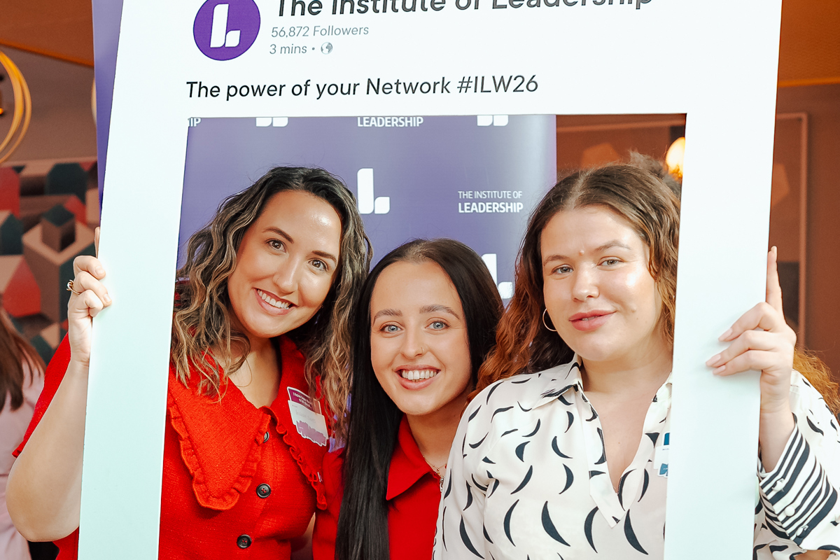 Three women smiling inside a large LinkedIn-style photo frame at a leadership event. The atmosphere is cheerful and professional.
